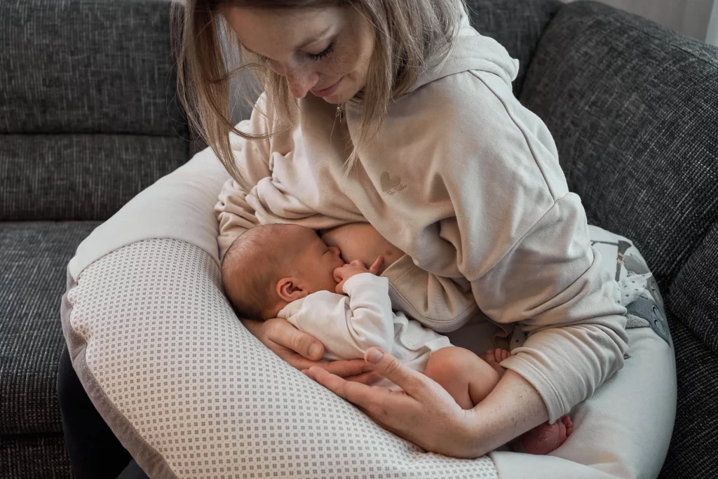 Mutter stillt das neugeborene Baby auf dem Stillkissen und blickt sanft lächelnd zum Baby.